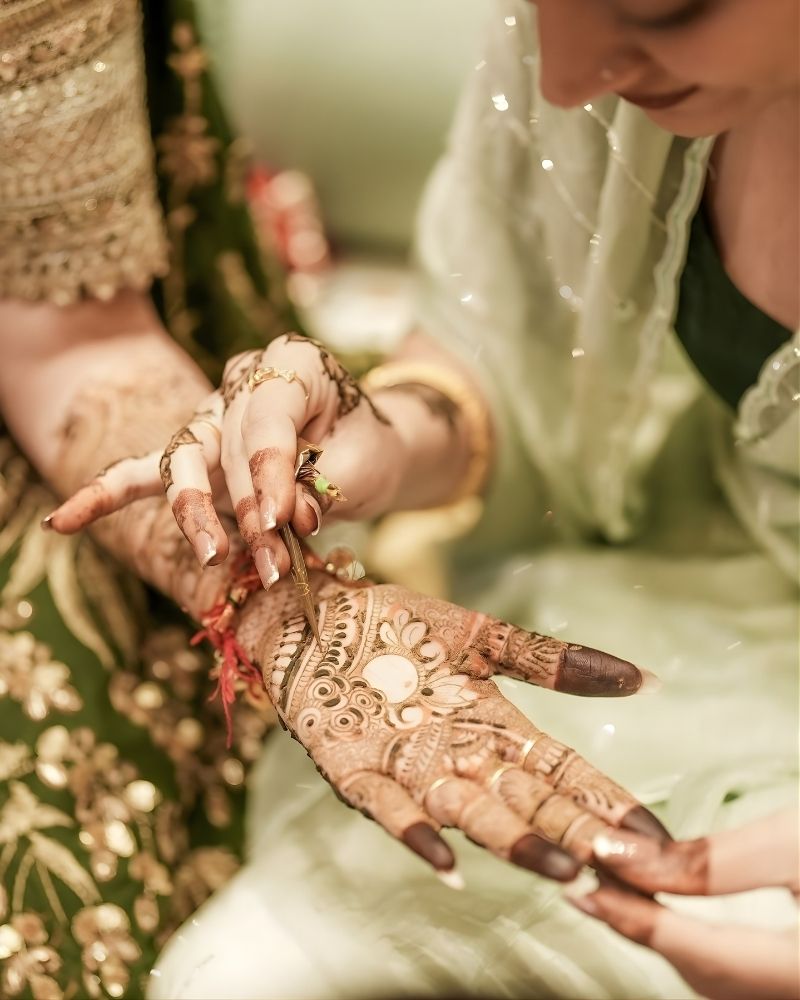 Bride sitting during a mehndi ceremony with fresh henna applied on hands